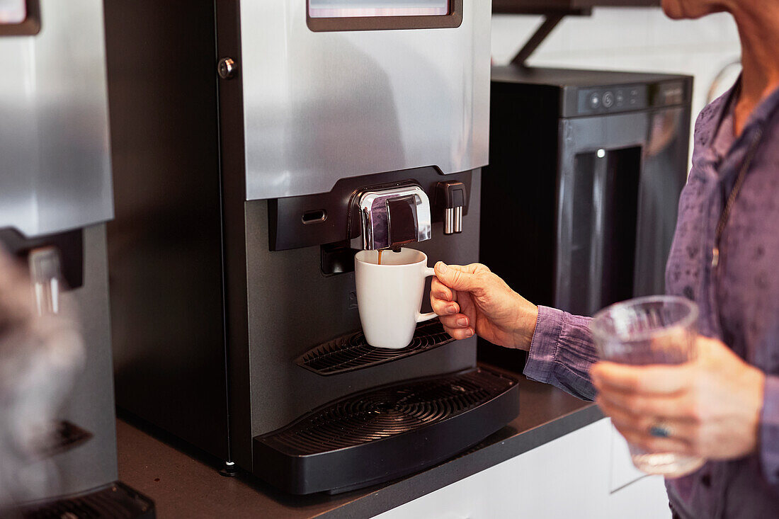 Frau bereitet Kaffee in der Büroküche zu