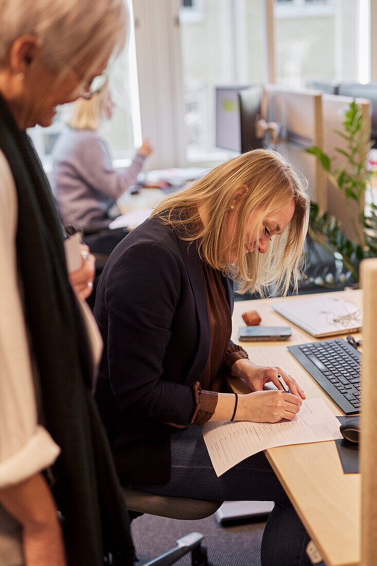 Lächelnde Frau beim Schreiben am Schreibtisch im Büro