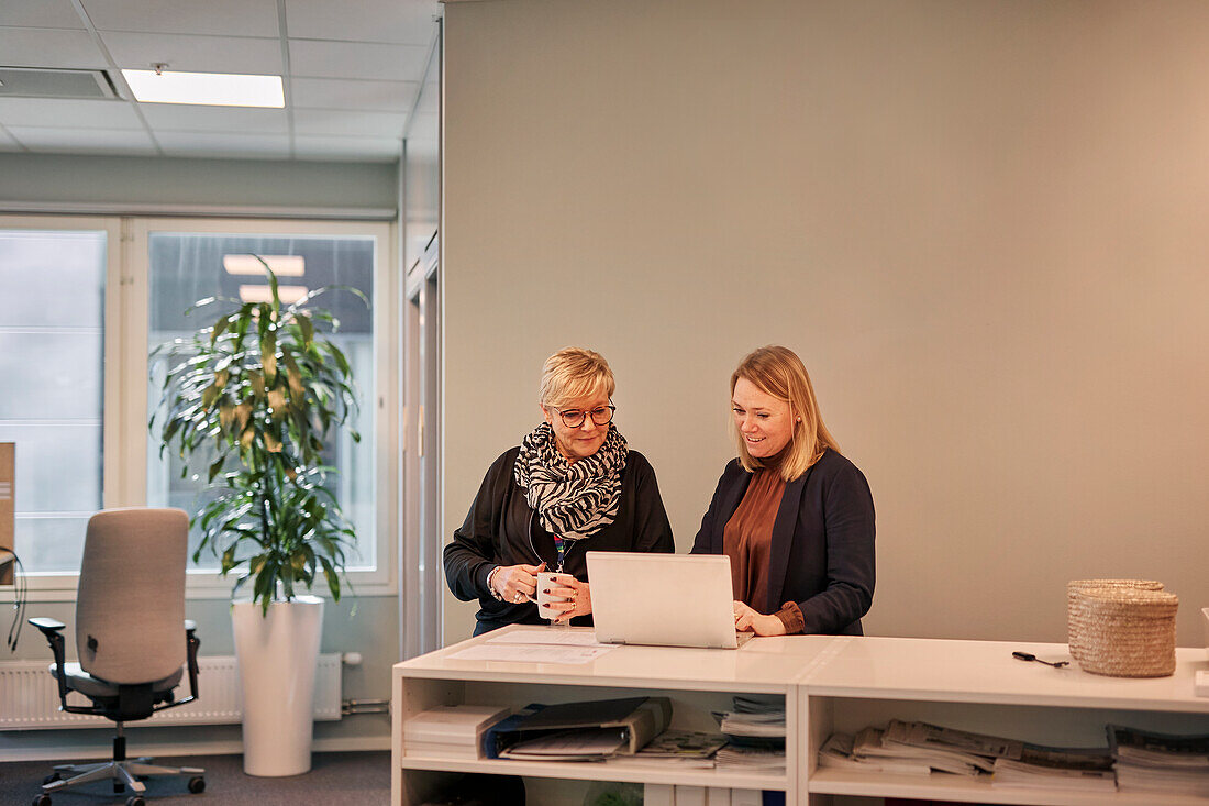 Lächelnde Frau im Büro, die einen Laptop benutzt