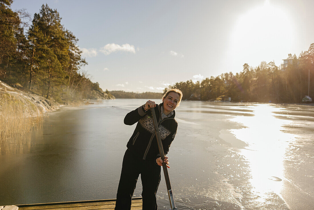 Lächelnde Frau am See, die eine Eissäge benutzt