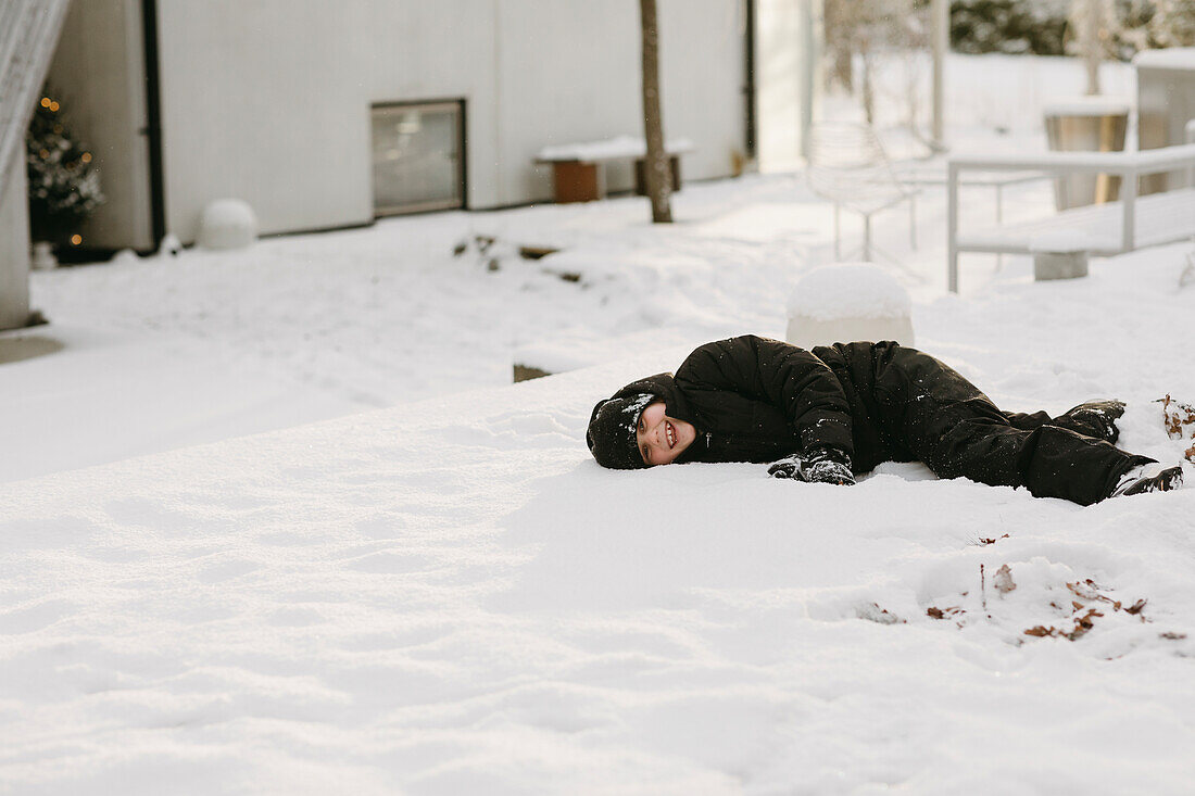 Lächelnder Junge im Schnee liegend im Winter