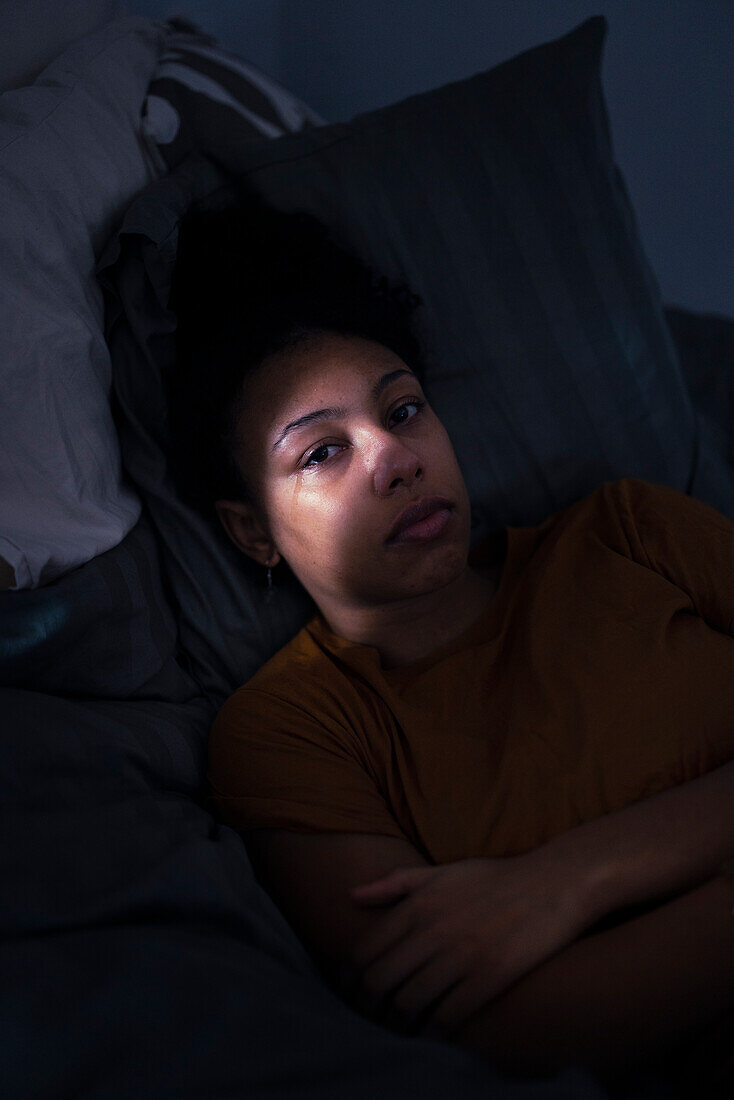 Portrait of crying young woman lying in bed