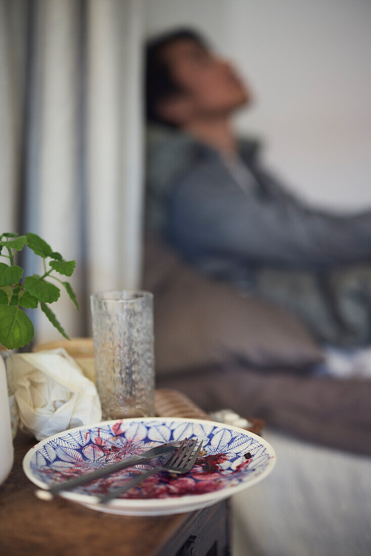 Schmutziger Teller auf dem Nachttisch und trauriger Mann mit Depressionen im Hintergrund