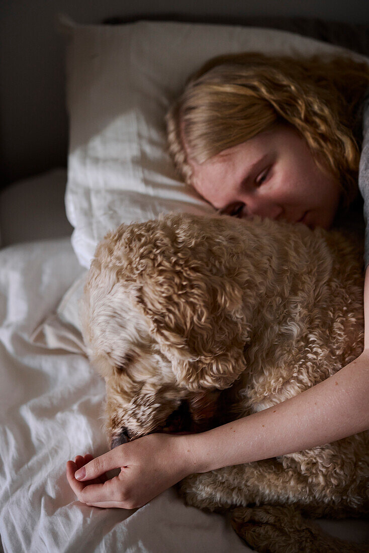 Crying young woman hugging dog in bed