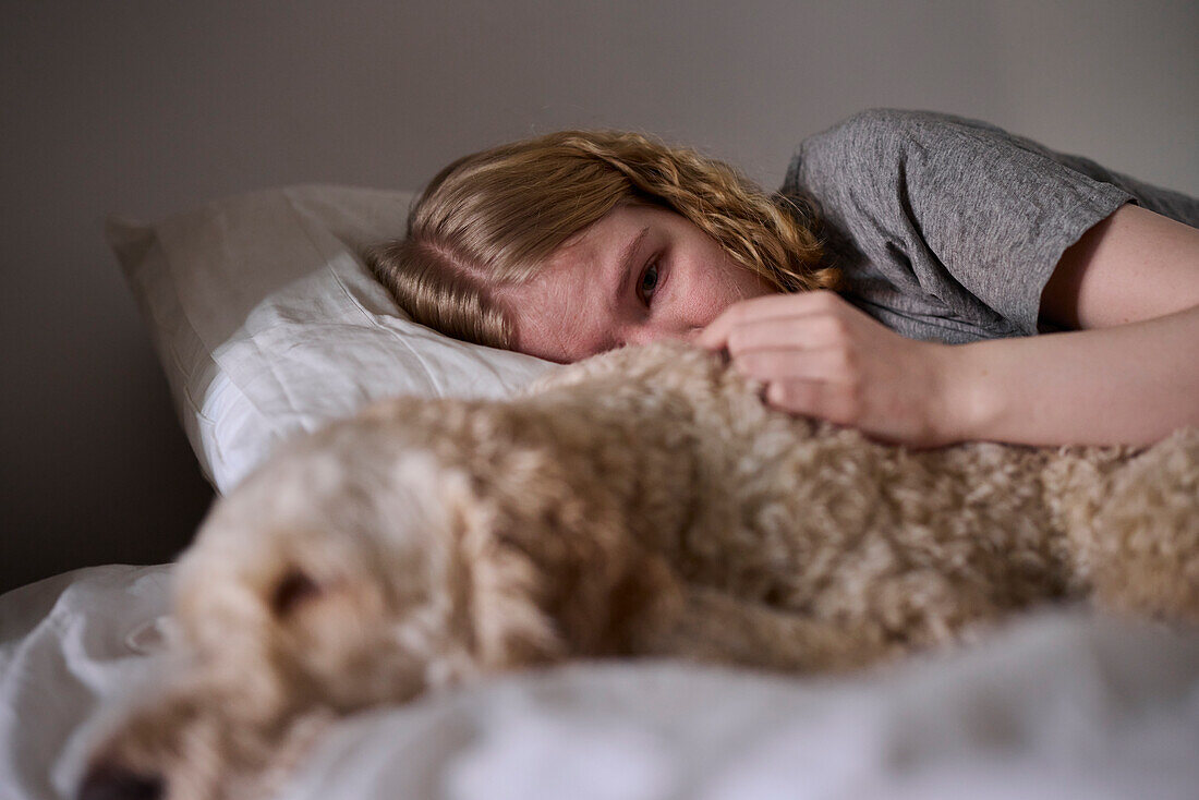 Weinende junge Frau umarmt Hund im Bett