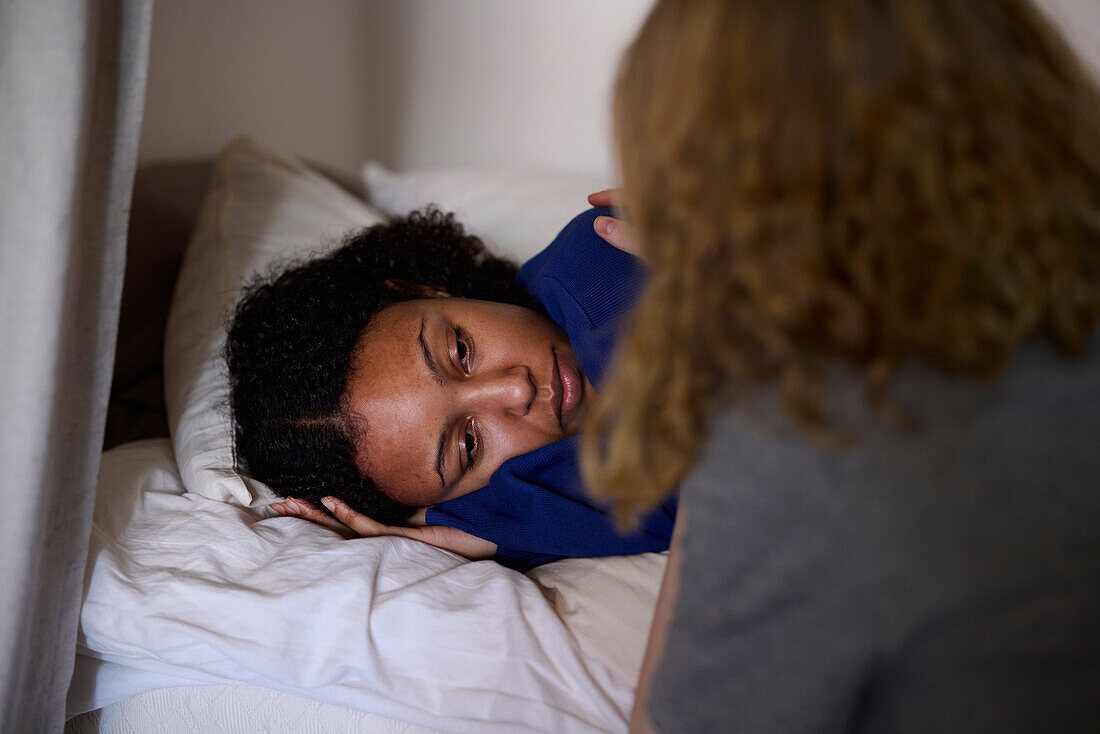 Young woman comforting friend lying in bed