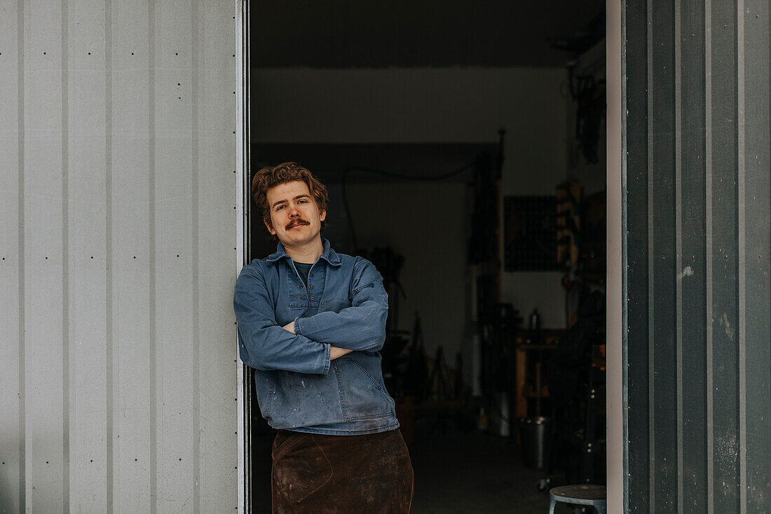 Porträt eines Schmieds, der im Eingang einer Werkstatt steht