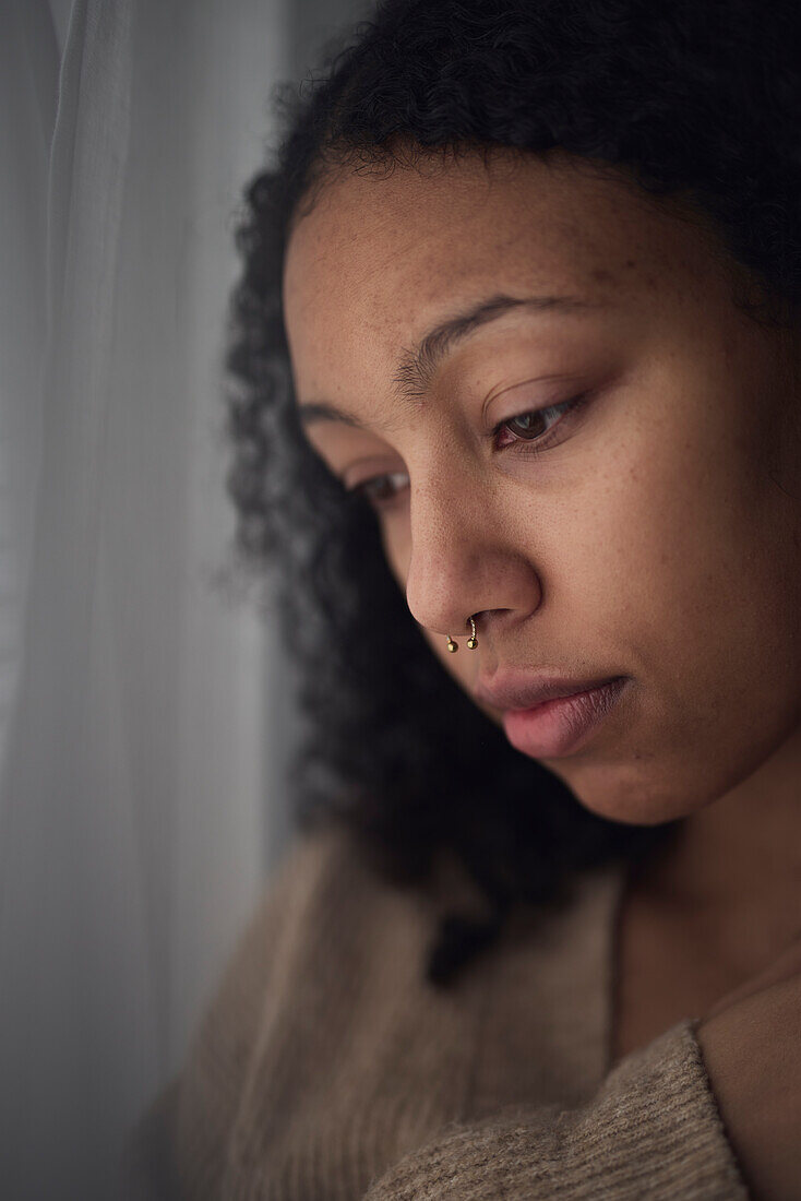 Pensive young woman looking through window