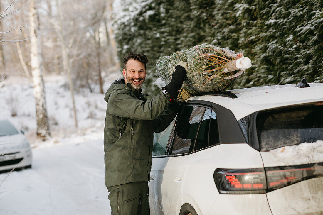 Mann legt Weihnachtsbaum auf Autodach