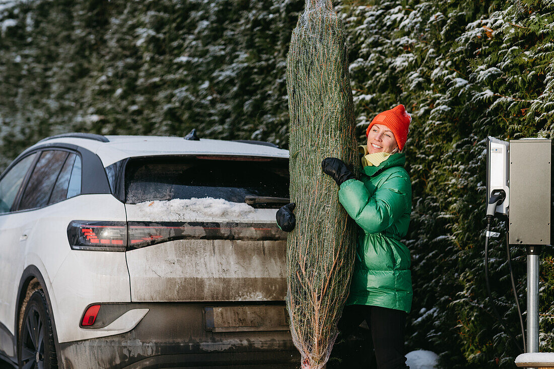 Smiling woman standing with Christmas tree near car