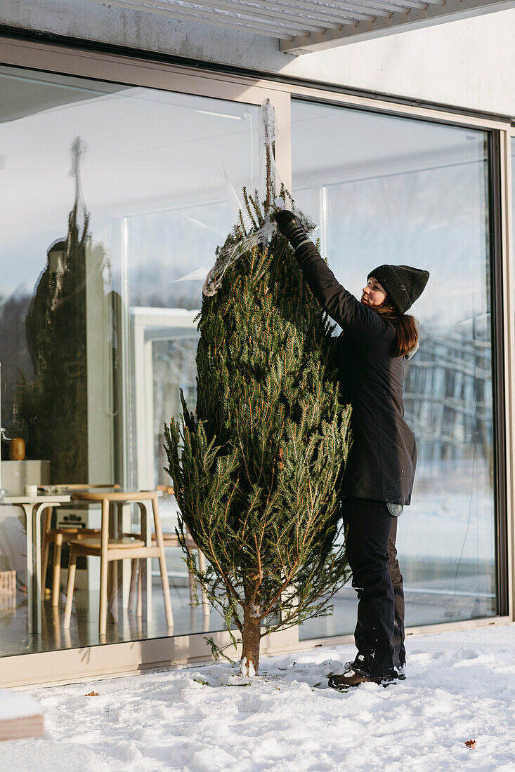 Frau bereitet Weihnachtsbaum vor dem Haus vor