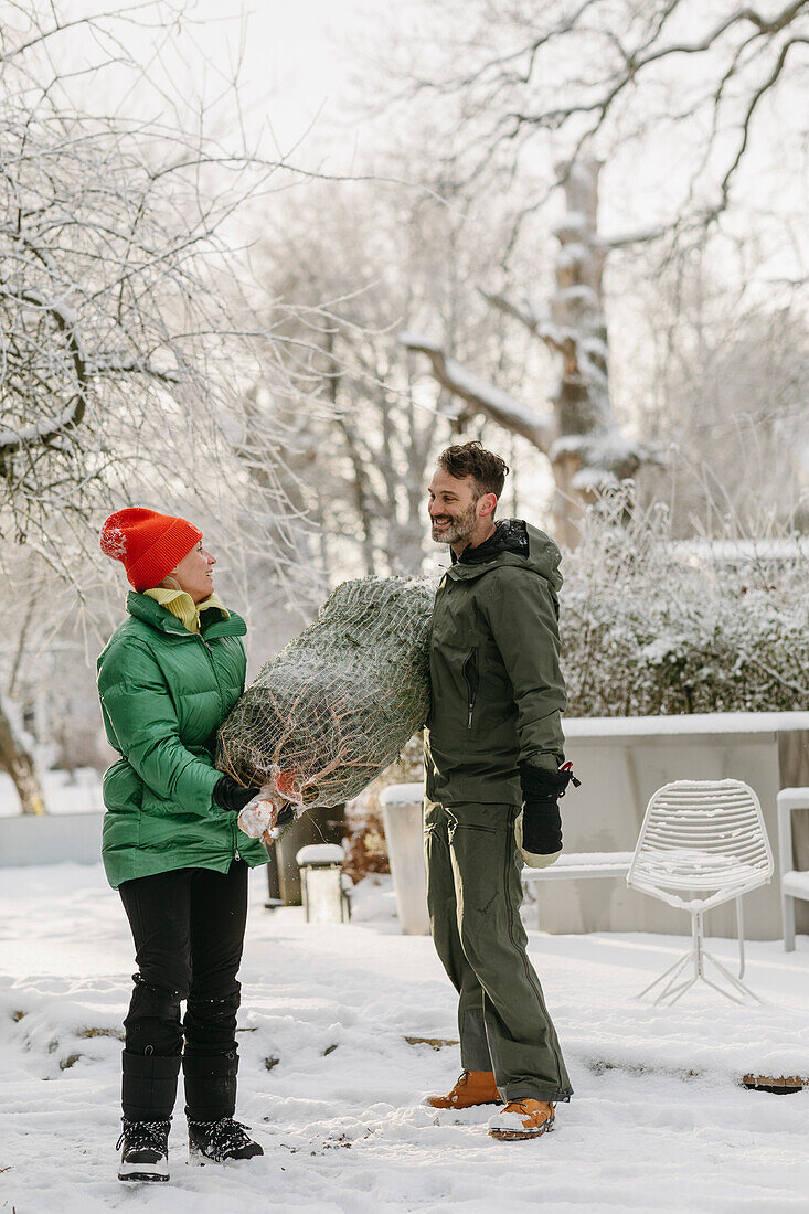 Man and woman carrying Christmas tree at winter