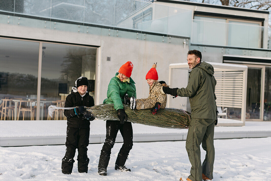 Familie trägt Weihnachtsbaum im Winter