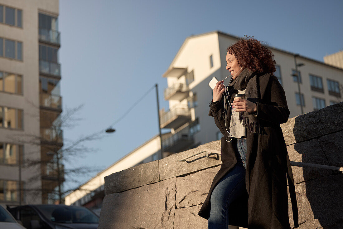 Beautiful woman with takeaway coffee and smartphone on street