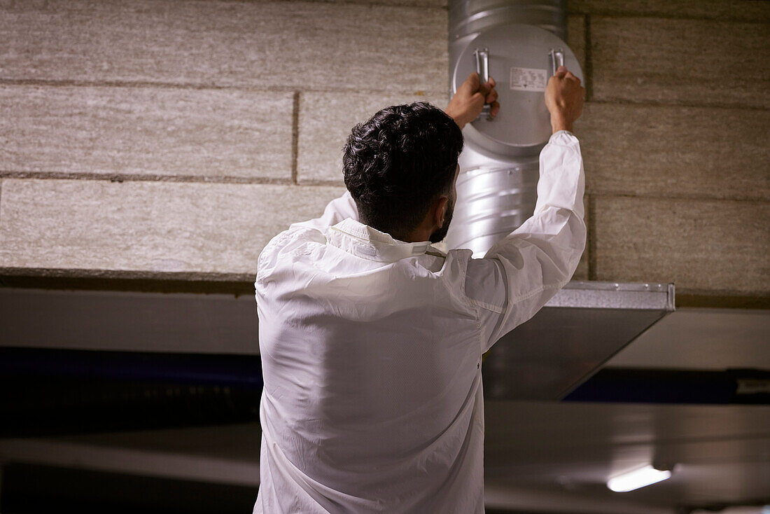 Rear view of man checking air duct