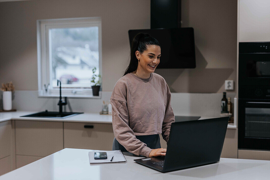 Smiling woman in kitchen using laptop