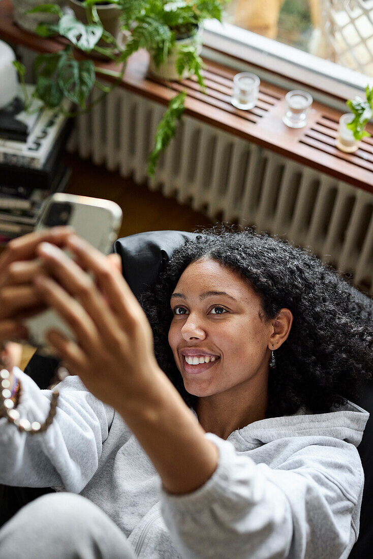 Lächelnde junge Frau, die auf einem Sitzsack liegt und ein Selfie macht