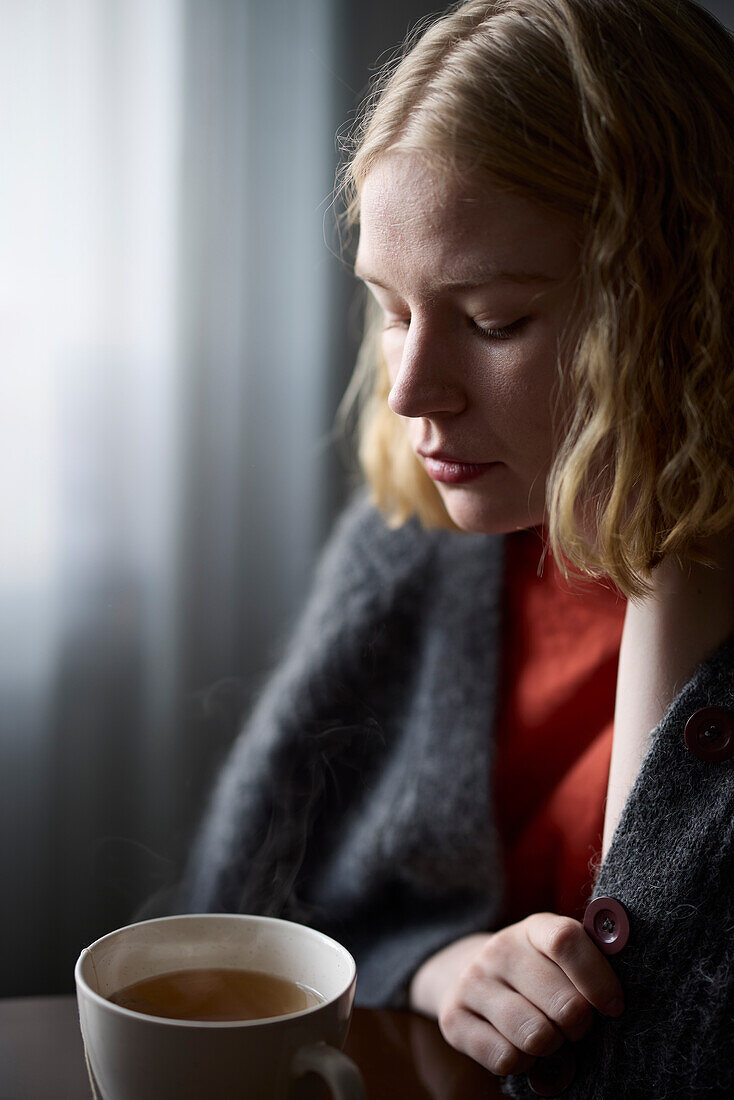 Nachdenkliche Teenagerin sitzt mit einer Tasse Tee am Tisch