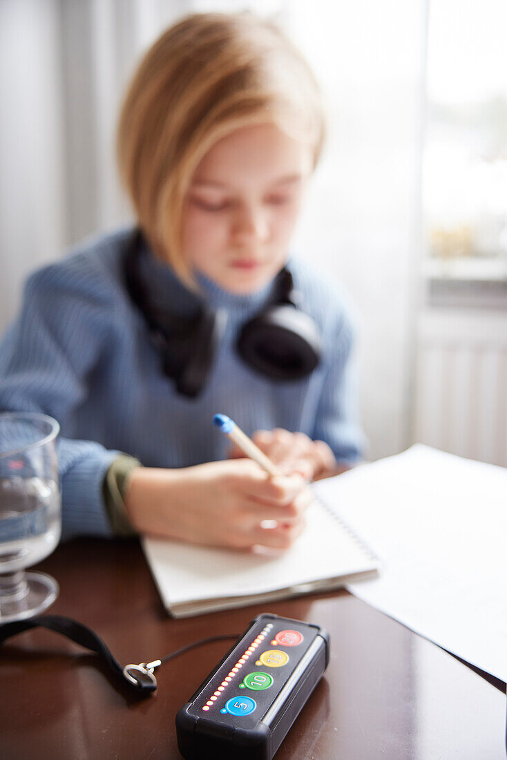 Electronic game on table, girl doing homework in background