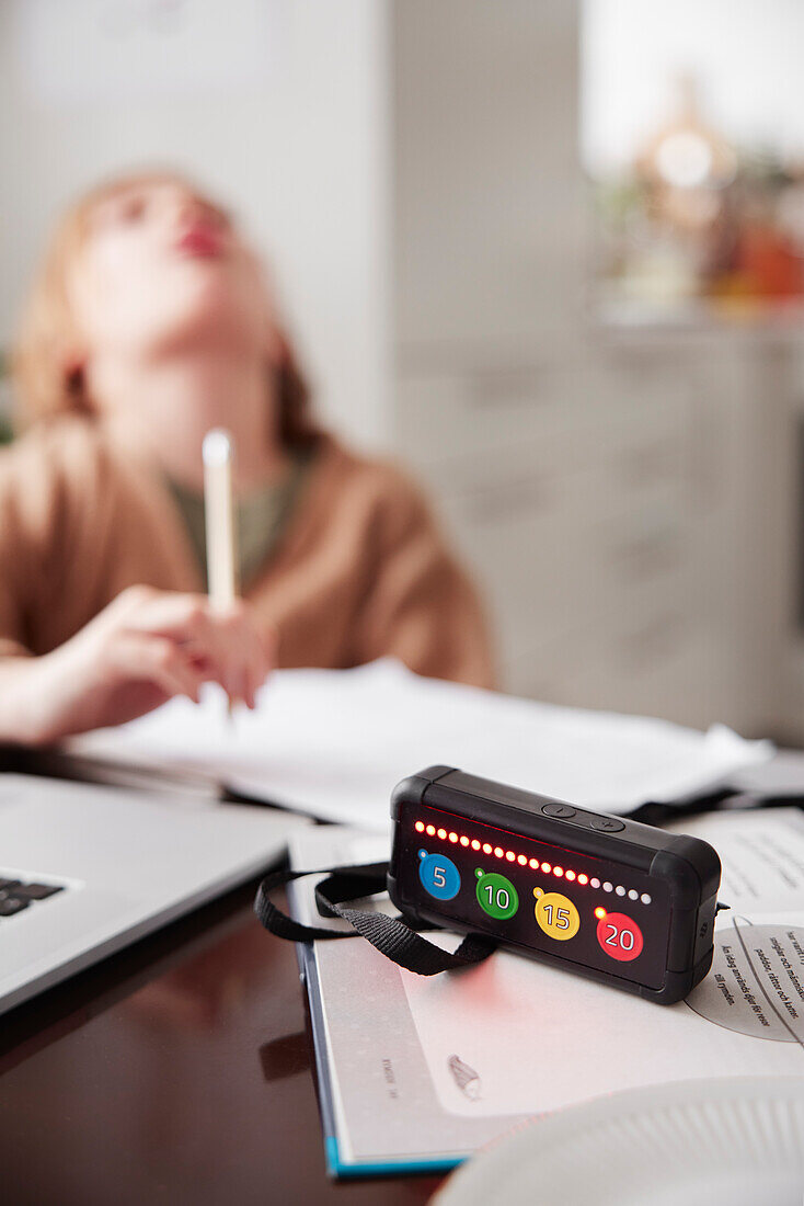 Electronic game on table, girl doing homework in background