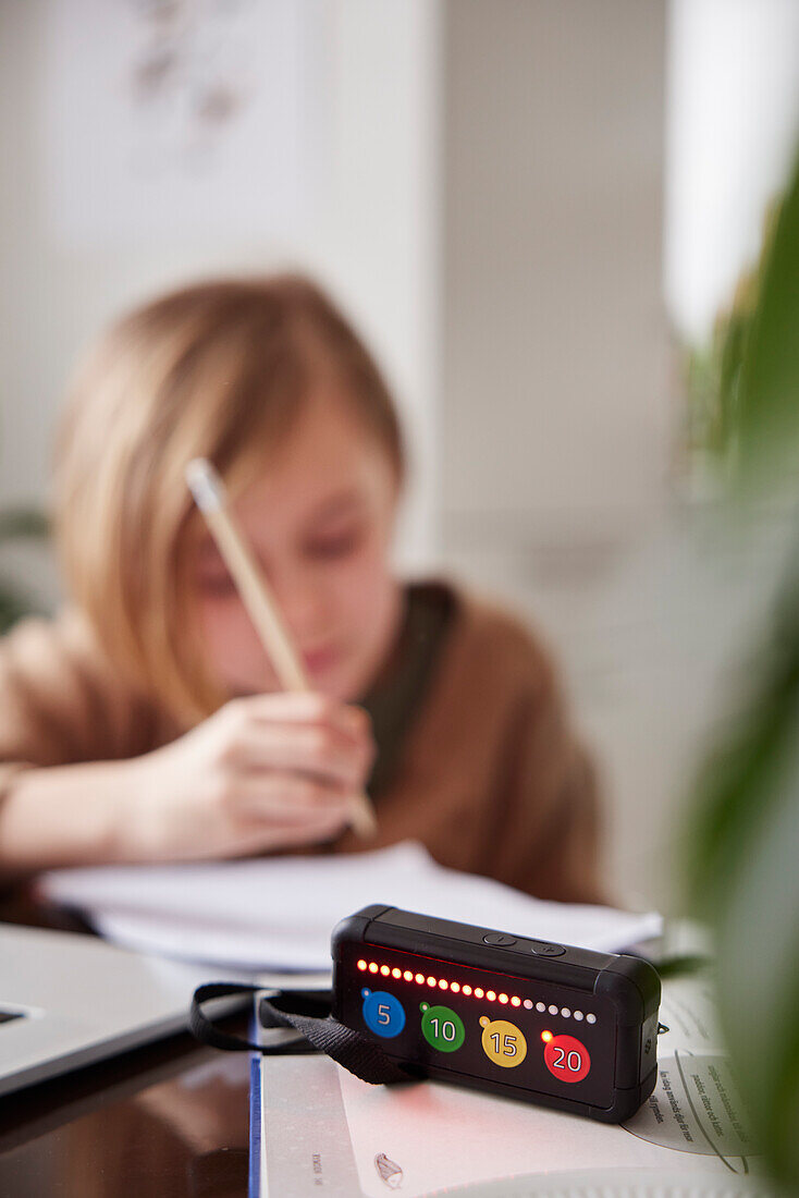 Electronic game on table, girl doing homework in background