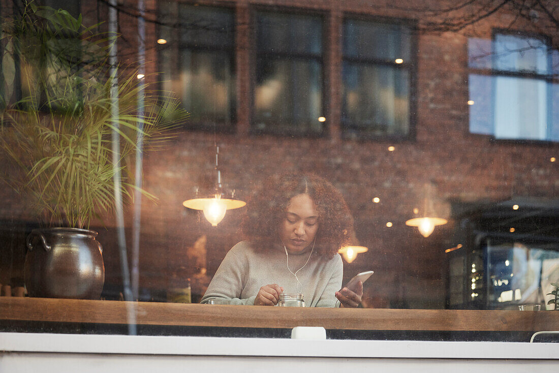 Young woman using cell phone and eating in cafe