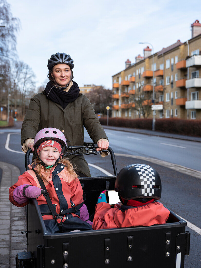 Young mother cycling with two children in cargo bicycle