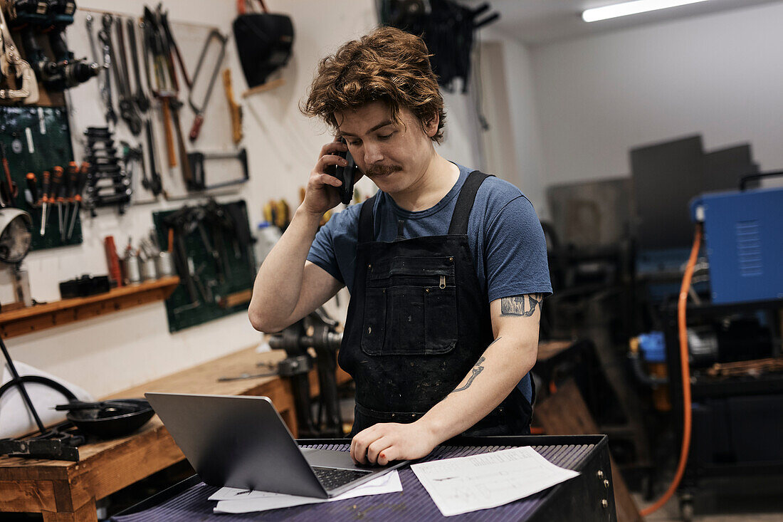 Blacksmith working with laptop and smartphone in his workshop