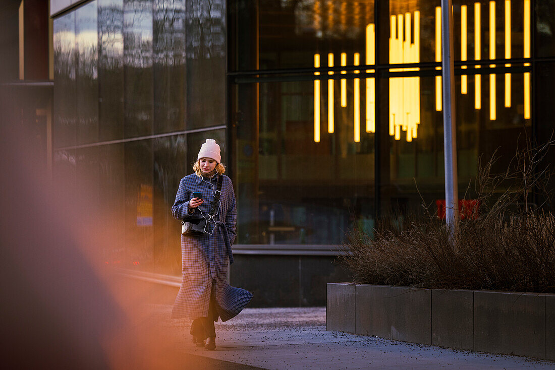 Young woman walking outdoors and using phone