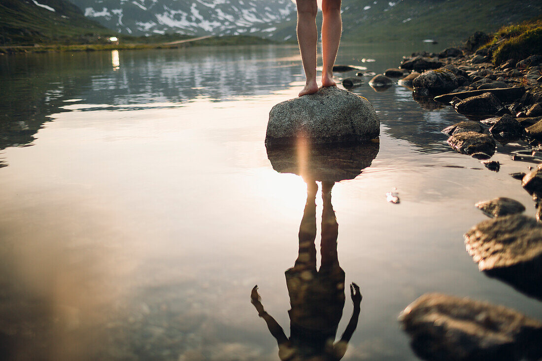 Low section of person standing on rock at lake