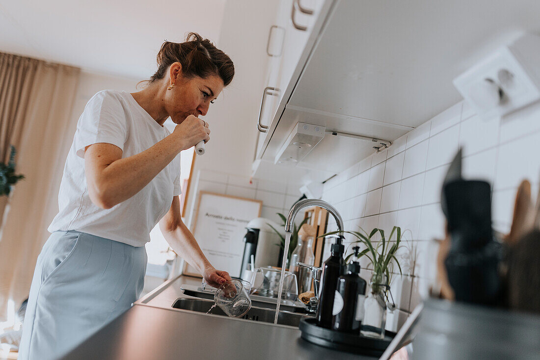 Woman brushing teeth at kitchen sink