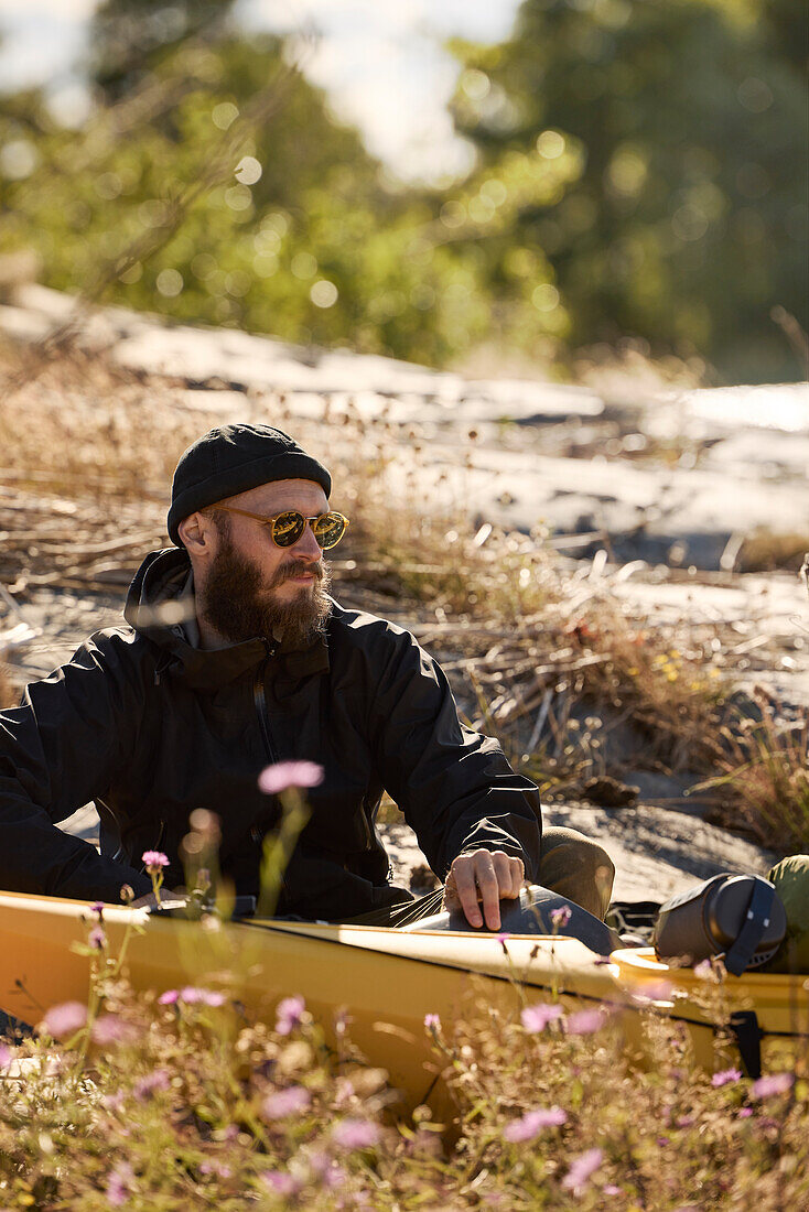 Man sitting near kayak on rocky coast