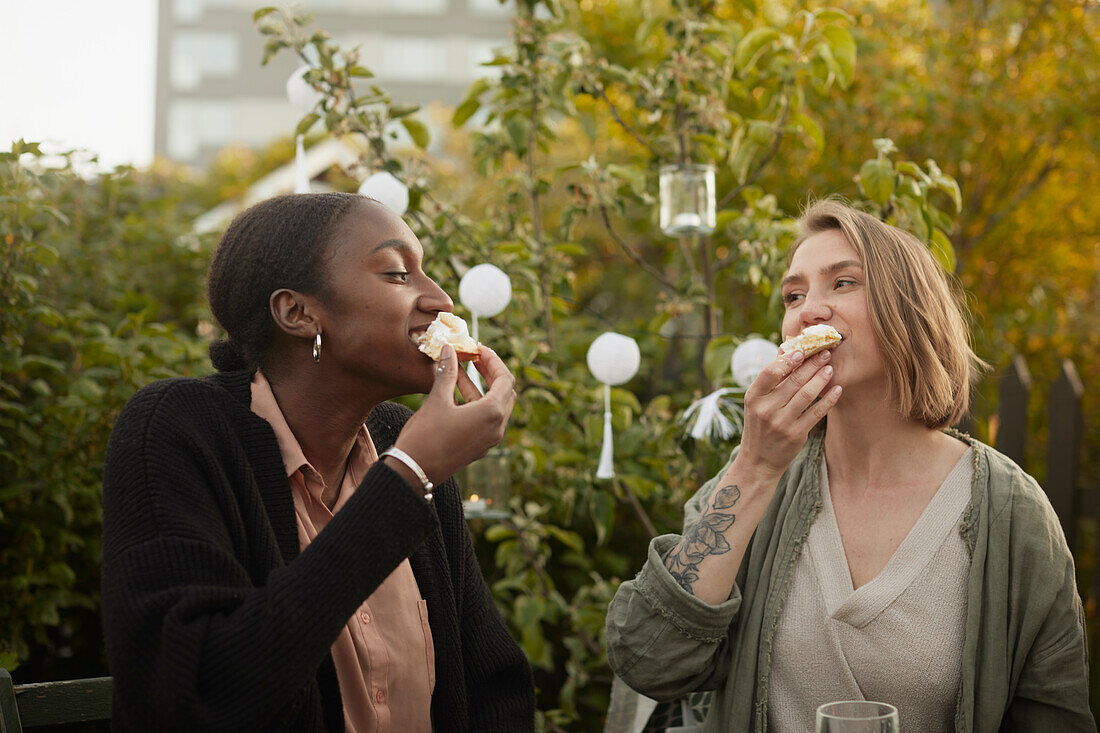 Smiling women eating cake in garden