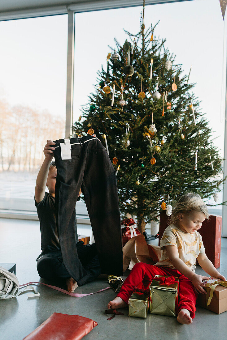 Brother and sister opening Christmas presents under Christmas tree