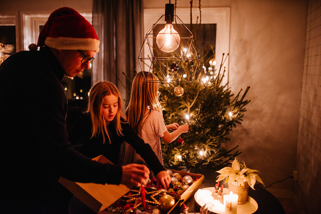 Vater und Töchter beim Schmücken des Weihnachtsbaums