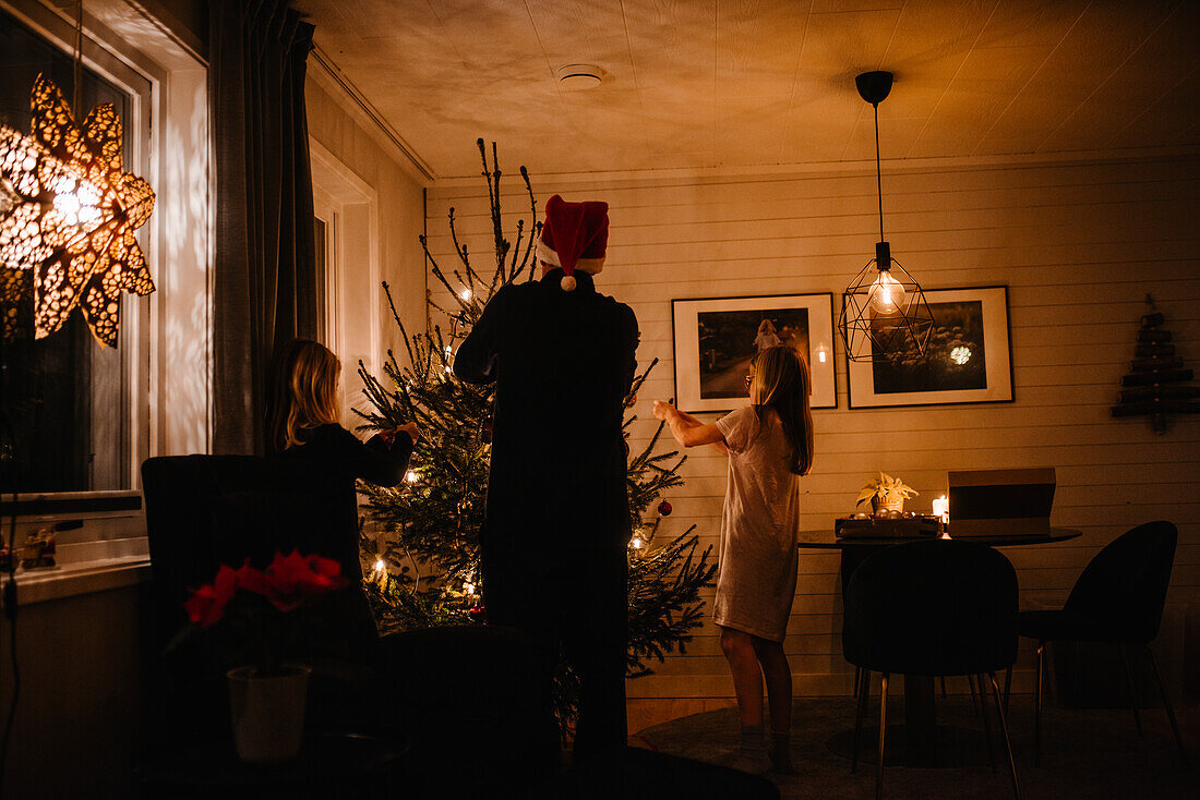 Vater und Töchter beim Schmücken des Weihnachtsbaums