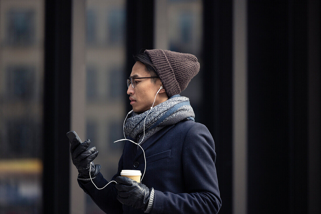 Gut aussehender Mann mit Smartphone und Pappbecher auf der Straße