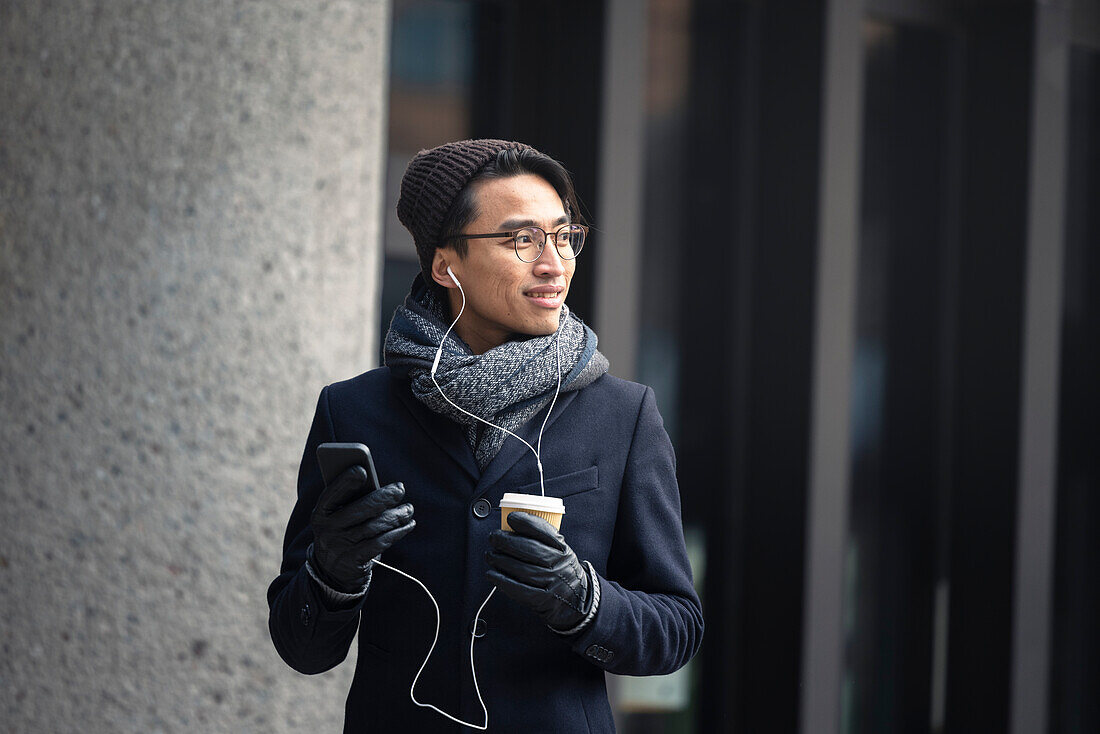 Handsome man with smartphone and paper cup on street