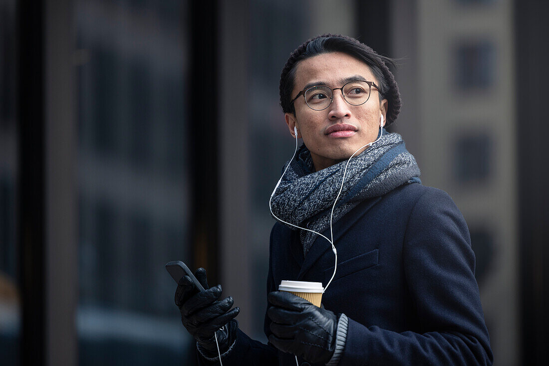 Handsome man with smartphone and paper cup on street