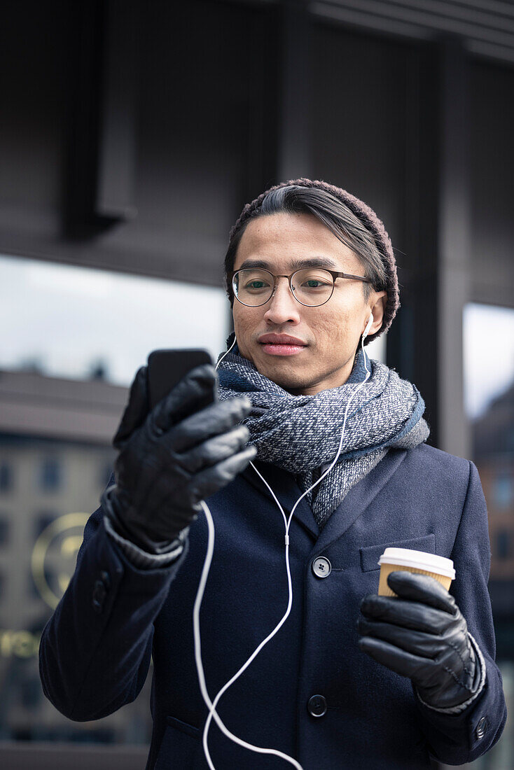 Handsome man with smartphone and paper cup on street