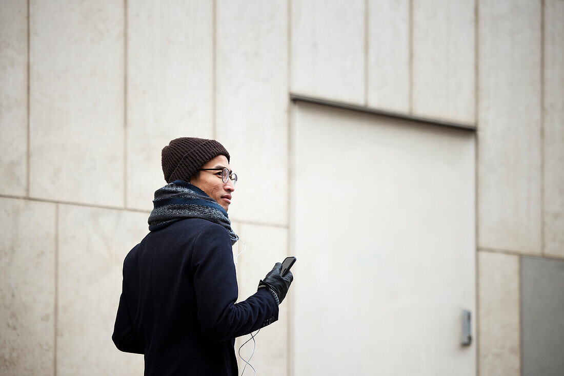 Lächelnder Mann hält Mobiltelefon beim Gehen