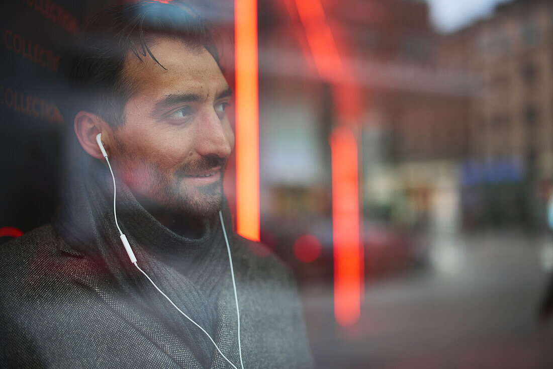 Eleganter Mann mit Ohrstöpseln, die sich im Fenster spiegeln