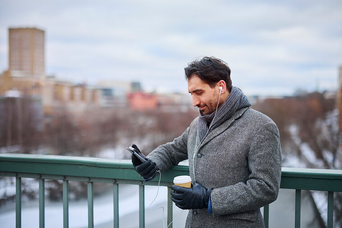 Elegant man with smartphone and paper cup on footbridge