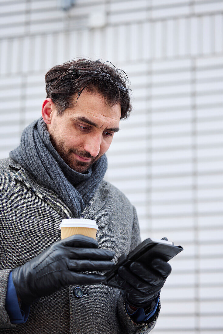 Eleganter Mann mit Smartphone und Pappbecher auf der Straße