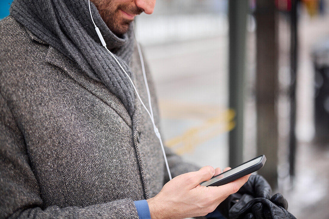 Eleganter Mann mit Smartphone wartet an der Bushaltestelle