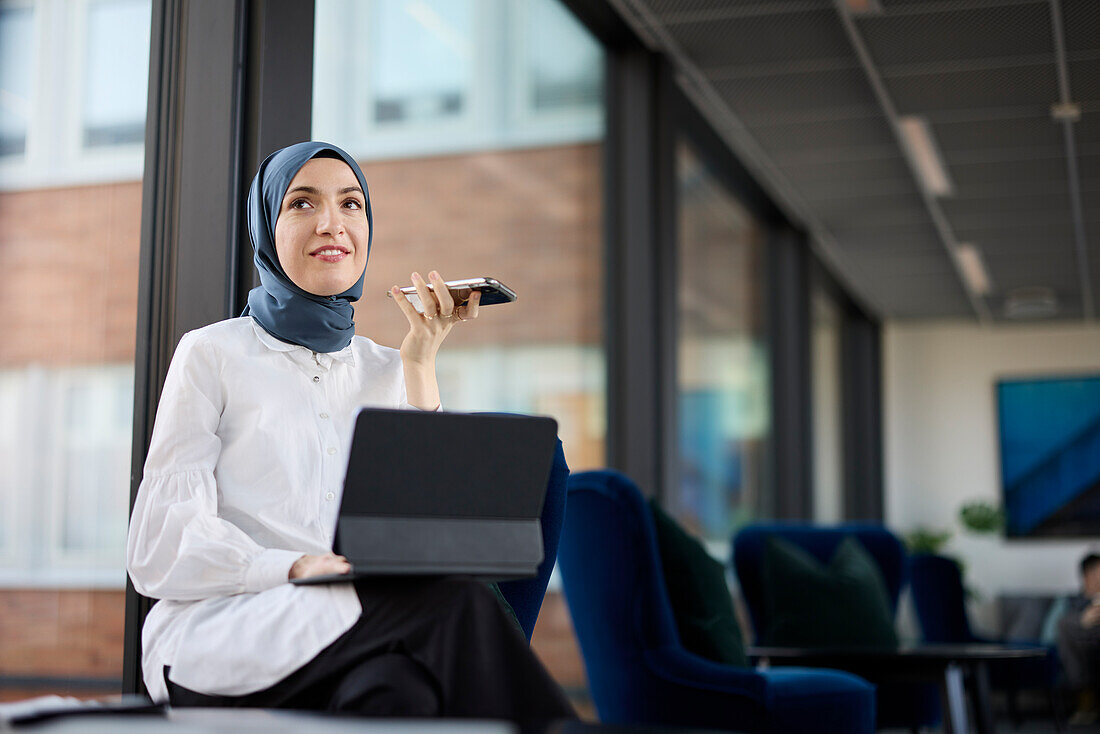 Geschäftsfrau im Hijab mit Telefon und digitalem Tablet im Büro