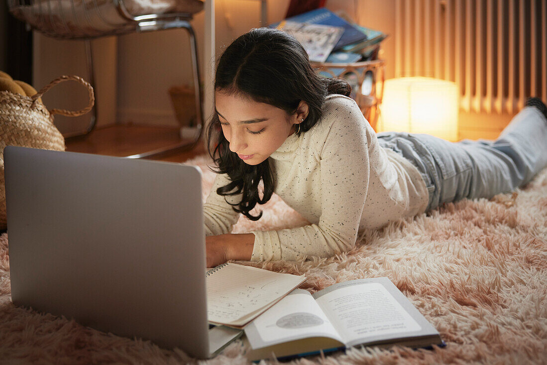 Mädchen macht Hausaufgaben mit Laptop auf dem Boden in ihrem Schlafzimmer