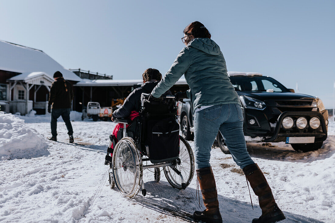Mutter beim Winterspaziergang mit Kind im Rollstuhl