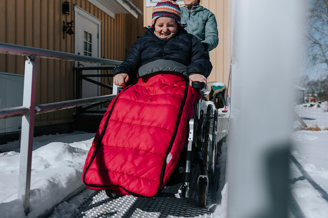 Eltern beim Winterspaziergang mit Tochter im Rollstuhl