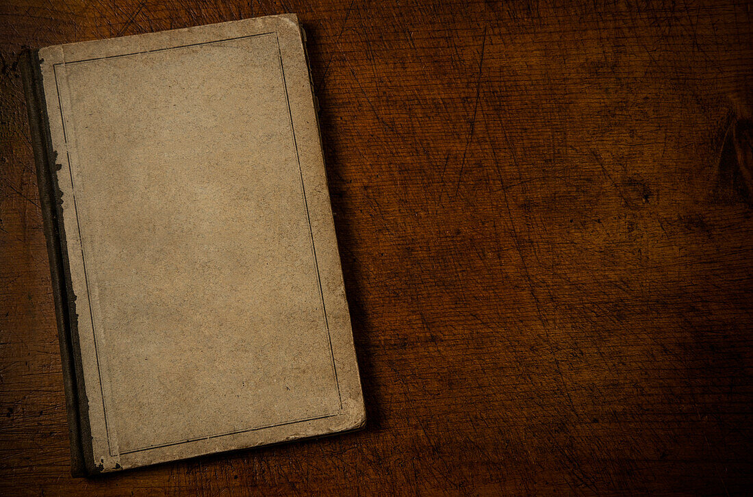 Altes Buch mit unbedrucktem Einband auf einer alten hölzernen Schreibtischplatte